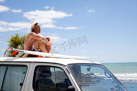 在海滩上成熟的男子带着冲浪板在车顶上观看