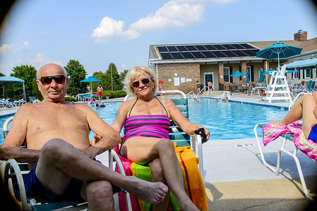 微笑的老年夫妇坐在室外游泳池边的肖像