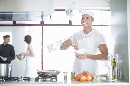 钵摄影照片_面带微笑的男厨师在商业厨房里用研钵和筷子搅拌