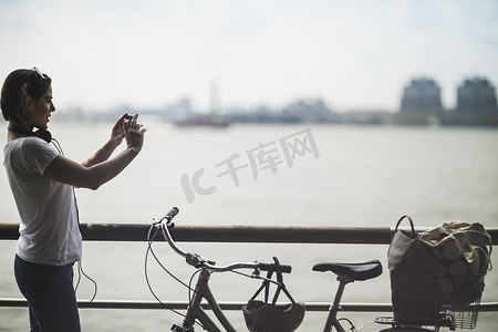 车联网摄影照片_中年女性骑车者在美国纽约市河滨用智能手机拍照
