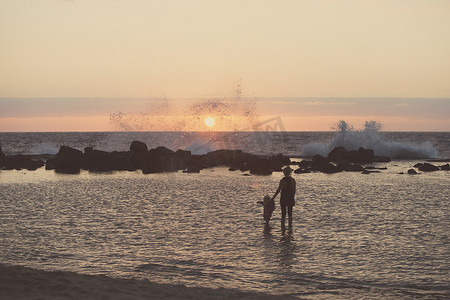 儿童培育摄影照片_美国夏威夷科纳轮廓分明的母亲和蹒跚学步的女孩子在海里划桨看着海浪飞溅