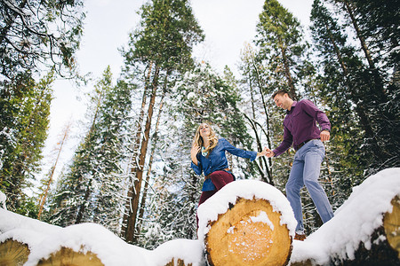 森林里的一对夫妇在积雪覆盖的原木上攀登