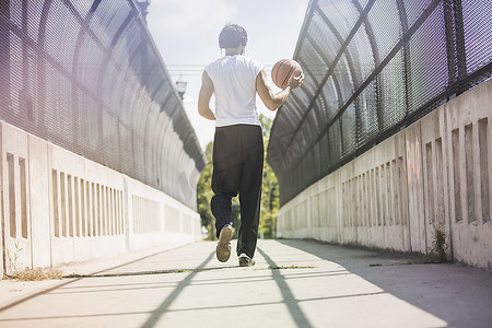 年轻男子篮球运动员背着球走在人行桥上的背影