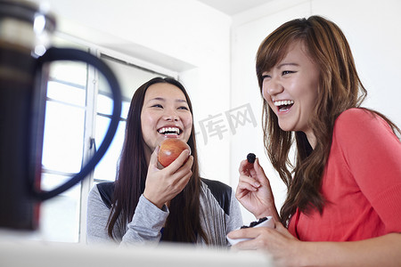 动物吃水果摄影照片_两名年轻女子在厨房里吃水果
