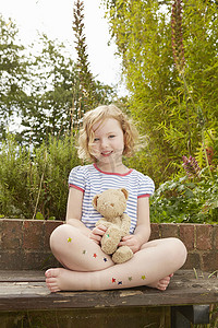 毛绒星星摄影照片_花园座椅上的女孩肖像腿上有泰迪熊和星星贴纸