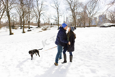 美国纽约中央公园一对浪漫的年轻夫妇抱着狗一起站在雪地里