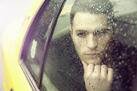 一名年轻男子在雨中凝视着黄色出租车车窗外