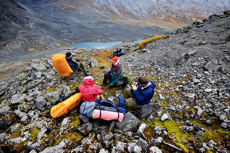 四名成年徒步旅行者在俄罗斯科拉半岛希比尼山脉崎岖的山谷景观中休息