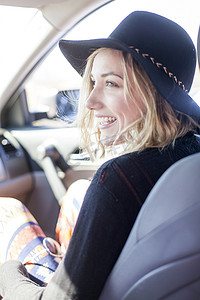 年轻的金发女子戴着帽子坐在车里微笑