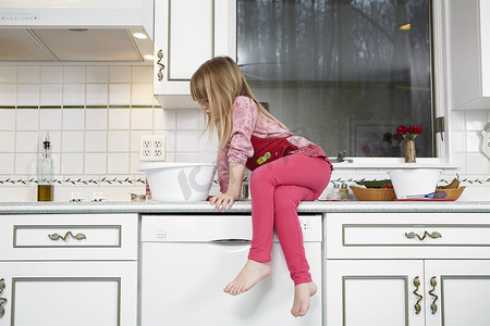 搅拌碗摄影照片_坐在厨房柜台上看着搅拌碗的女孩