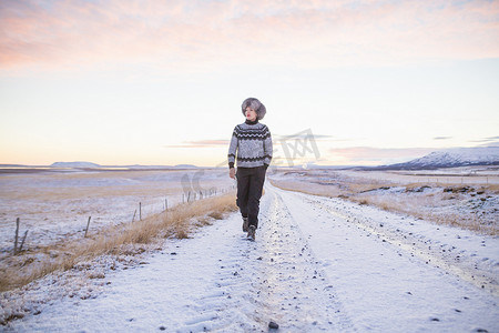 冰岛一名女子走在积雪覆盖的乡村道路上