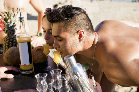美国加利福尼亚州纽波特海滩一对年轻男女身体前倾喝鸡尾酒