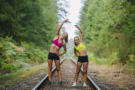 对称摄影照片_年轻女子和十几岁的女孩在乡村铁轨上锻炼
