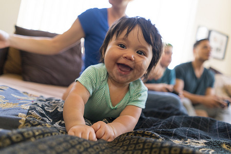 爱情发生摄影照片_婴儿在沙发上灿烂地笑着背景是家人