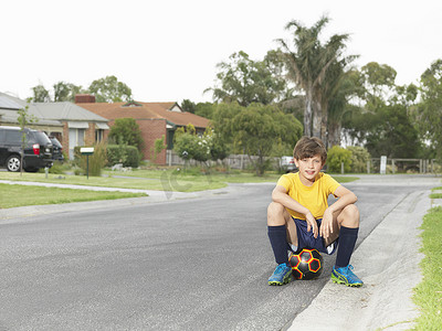 郊区道路上坐在足球上的男孩肖像