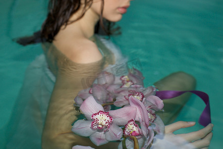 年轻女子在温泉游泳池里和一束紫色兰花的剪影