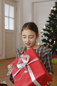 圣诞树亮摄影照片_圣诞树前的女孩低头拿着礼物