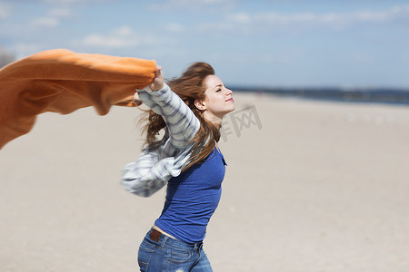 民族风背景摄影照片_一名年轻女子在多风的海滩上举着毯子