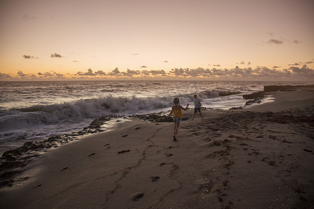 男孩和妹妹在日出时在海滩上跑步美国佛罗里达州朱庇特岛吹石保护区