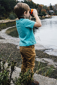 一个小男孩站在湖边用望远镜看着