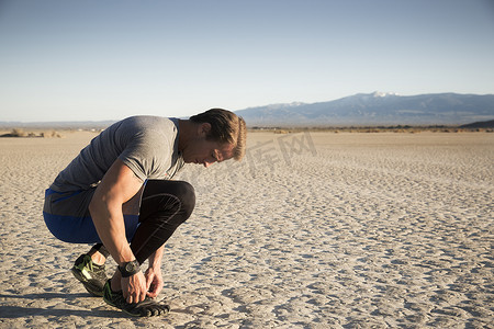 运动鞋摄影照片_美国加利福尼亚州埃尔米拉奇男子训练在干涸的湖床上系系教练鞋带