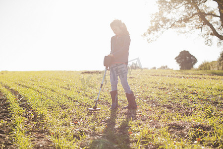 资源搜索摄影照片_戴着耳机的女孩在阳光明媚的田野上用金属探测器进行搜索