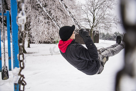 零下四度摄影照片_在零下30摄氏度的公园秋千上玩耍的年轻人