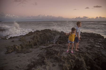 女孩和兄弟在日出时从海滩上眺望美国佛罗里达州朱庇特岛的吹石保护区