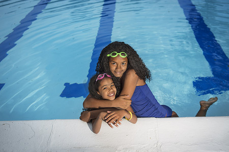 孩子游泳摄影照片_游泳池里的女孩抱着小妹妹微笑着看着镜头