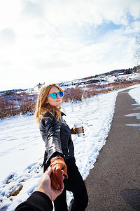 小路摄影照片_一名女子牵着男朋友在白雪覆盖的风景中散步