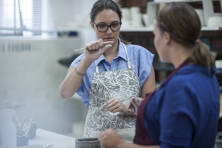 小动物举重摄影照片_女陶工在车间向学员讲解工具