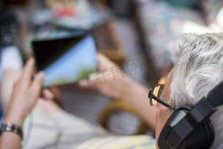 便携式摄影照片_老人坐在家里戴着耳机使用数字平板电脑俯瞰