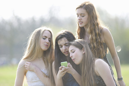 十几岁的少女摄影照片_四名十几岁的女孩在公园看智能手机短信