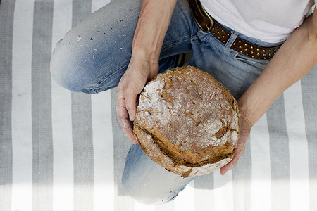 烘焙面包摄影照片_俯瞰坐在条纹地毯上的成熟女子手持新鲜烘焙面包