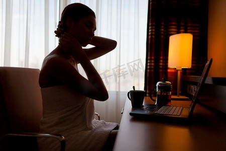 咖啡壶摄影照片_一名年轻女子坐在酒店房间的笔记本电脑前