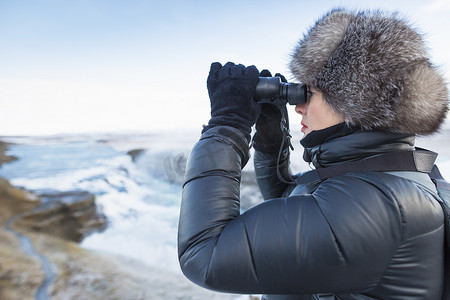 追逐摄影照片_一名女子用双筒望远镜观看位于冰岛西南部河峡谷中的瀑布