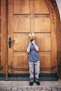 追逐摄影照片_男孩站在门口用智能手机拍照的全身正视图布卢登茨奥地利沃拉尔贝格