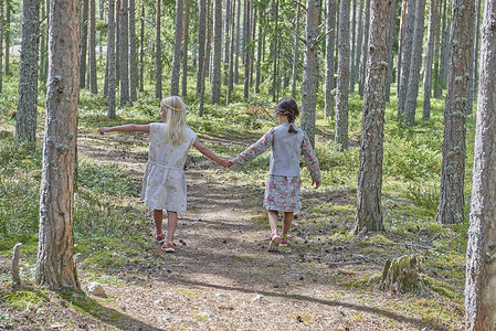 两个穿着复古服装的女孩手牵着手走在森林里的背影