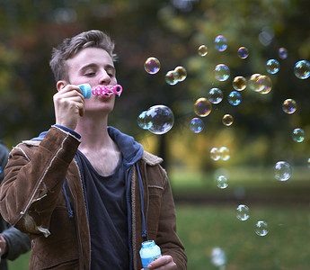 一位年轻男子在秋季公园吹泡泡