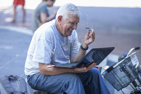 城市步行街上的一位老人边看笔记本电脑边笑