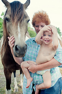 女性焦虑摄影照片_抱着小马的祖母和蹒跚学步的孩子