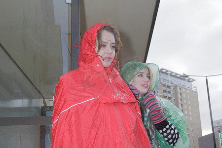 两名身穿雨衣的妇女在公交车站