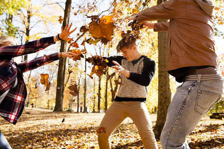 一位年轻女子和两个十几岁的兄弟在秋天的森林里互相扔树叶