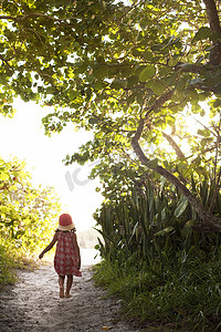 美国佛罗里达州安娜玛丽亚岛戴着太阳帽的赤脚女孩走在林地海滩小路上的背影