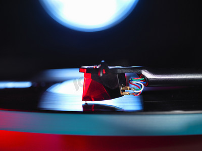 聚光灯点亮的转盘和播放黑胶唱片的红色指示笔的特写
