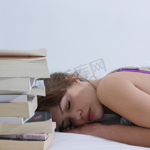 闭着眼睛摄影照片_睡在书边的年轻女子