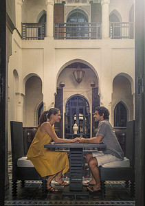 对称摄影照片_摩洛哥马拉喀什年轻夫妇面对面地坐在桌子旁手牵手的侧视
