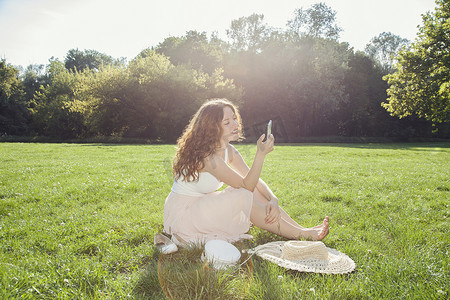 凯格尔摄影照片_坐在公园草地上看智能手机的年轻女子