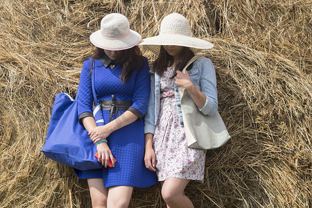 两名女性戴着太阳帽靠在干草上脸被遮住了