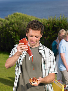 一名男子将番茄酱浇在热狗上